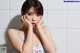 A woman in a blue dress sitting in a bathtub with her hands on her face.