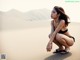 A woman in a black bikini sitting on a sand dune.